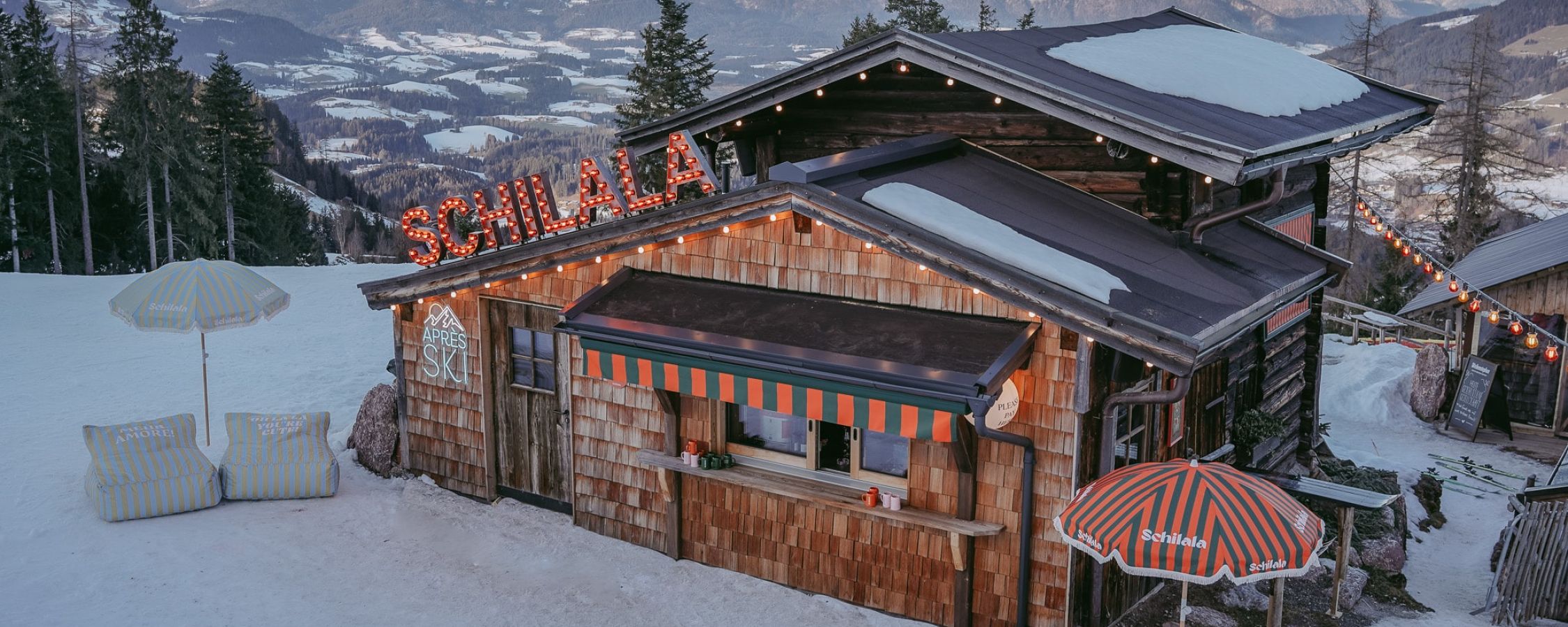 Blick auf die Schilala Hütte mit verschneitem Bergpanorama im Hintergrund.